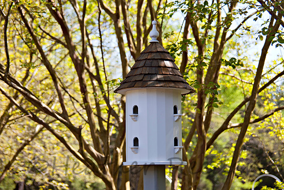Large, uniquely shaped birdhouse tower surrounded by lush green foliage.