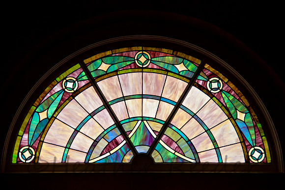 Colorful, elegant patterned stained glass window in circle top design.