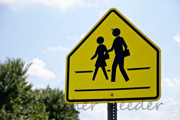 Yellow pedestrian crossing caution sign surrounded by blue cloudy sky.