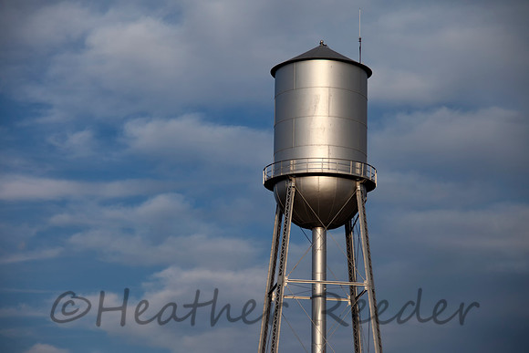 Tall silver water tower with cloudy blue sky background