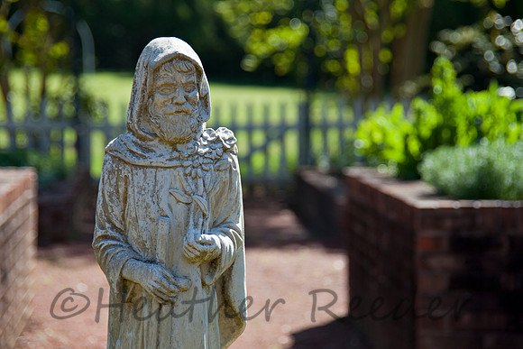 Delightfully aged garden statue surrounded by lush green foliage and garden pathway.