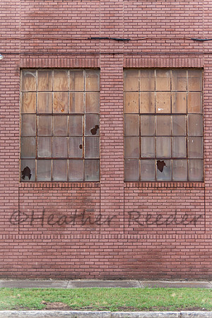 Old red brick building showing signs of abandonment with two busted windows.