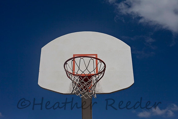 Retro recreational basketball goal surrounded by cloudy blue sky.