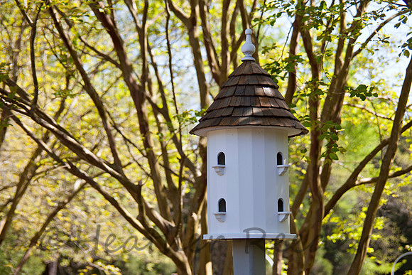 Large, uniquely shaped birdhouse tower surrounded by lush green foliage.