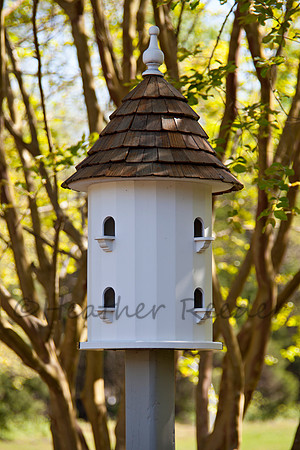 Large, uniquely shaped birdhouse tower surrounded by lush green foliage.