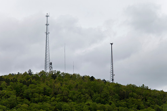 Various sized communication towers on lush green mountain top.